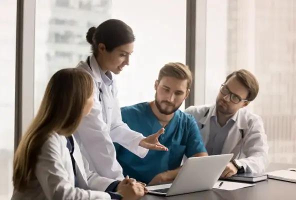 Medical professionals gathered in a meeting discussing patient care and practice strategies around a laptop in a hospital office.