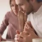 The image shows a couple sitting closely together at a table, looking concerned as they review paperwork, with a coffee cup and pen in front of them.