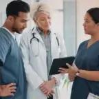 Three healthcare professionals, including a physician and two clinicians in scrubs, reviewing information together on a tablet in a clinical setting.