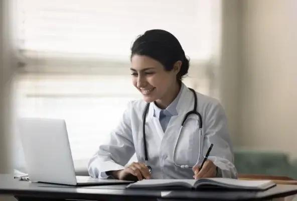 A smiling healthcare professional engages in online financial planning, representing modern practice management and efficiency.