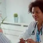 Smiling female doctor with a stethoscope talks to an older woman patient in a medical office.