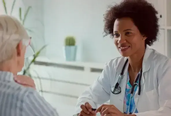 Smiling female doctor with a stethoscope talks to an older woman patient in a medical office.